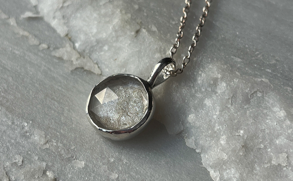 Silver pendant necklace with a faceted stone on a gray stone surface