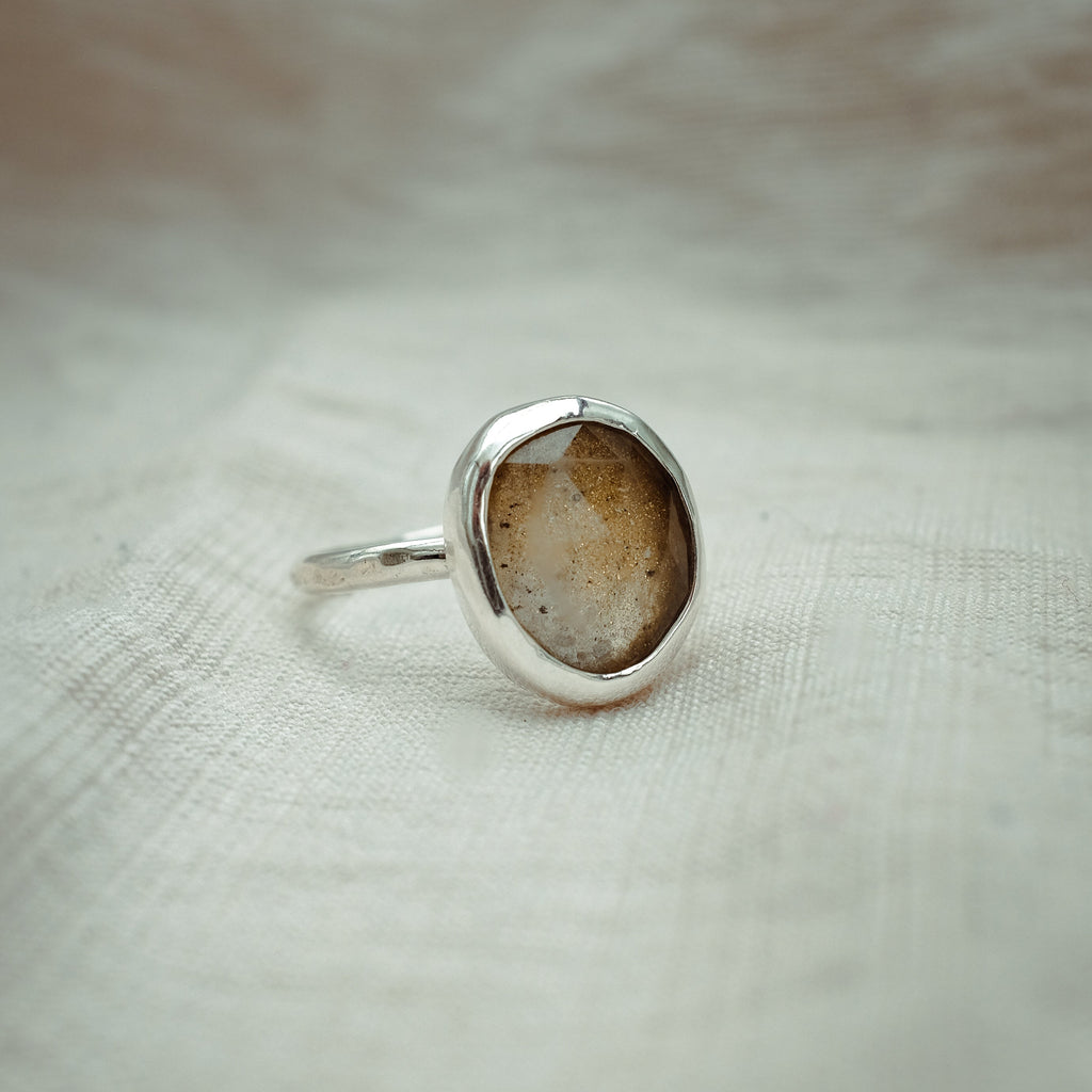Silver ring with a brown stone on a textured beige background