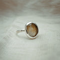Silver ring with a brown stone on a textured beige background
