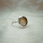 Silver ring with a brown stone on a textured beige background