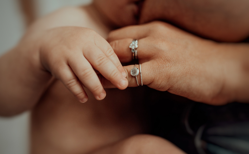 a finger print pressed silver ring, on a hand holding a baby's hand