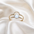 Gold ring with a light blue gemstone on a white satin background