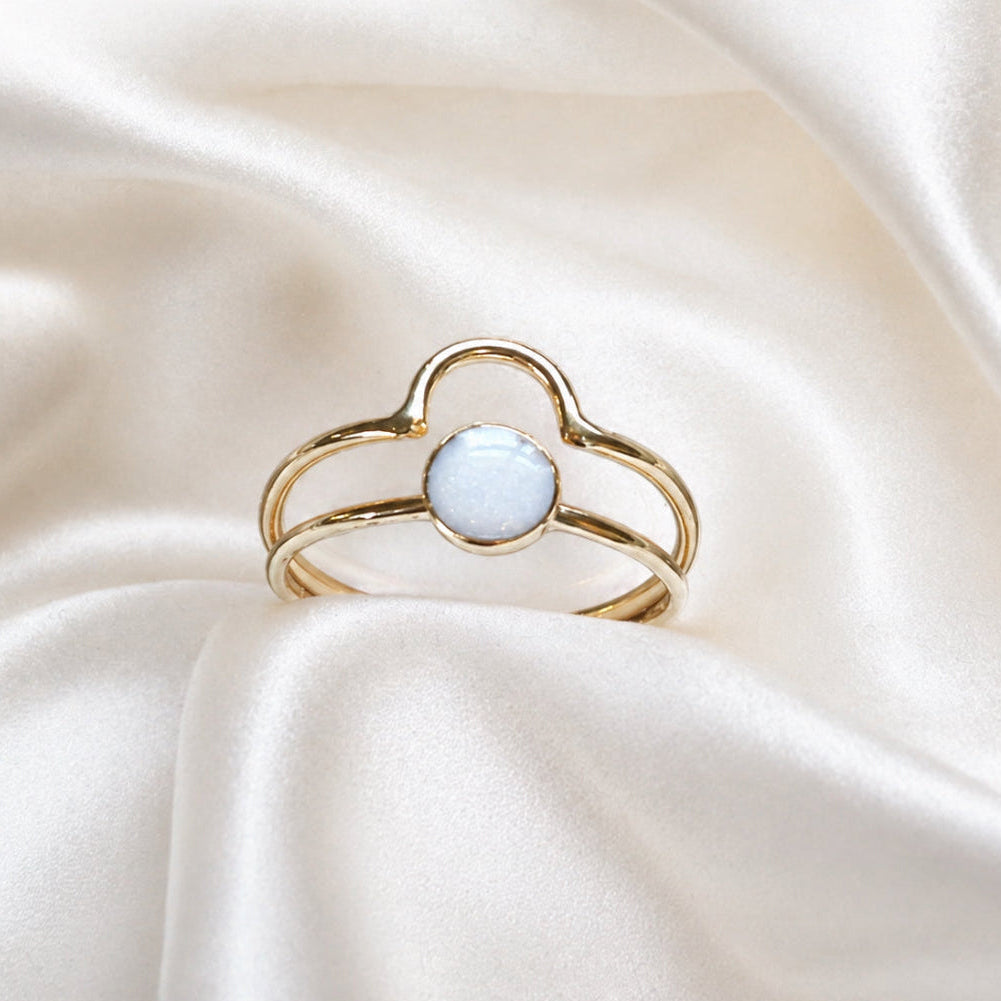 Gold ring with a light blue gemstone on a white satin background