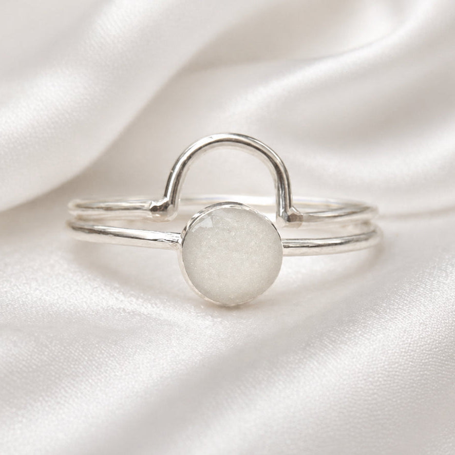 Silver ring with a circular design on a white satin background